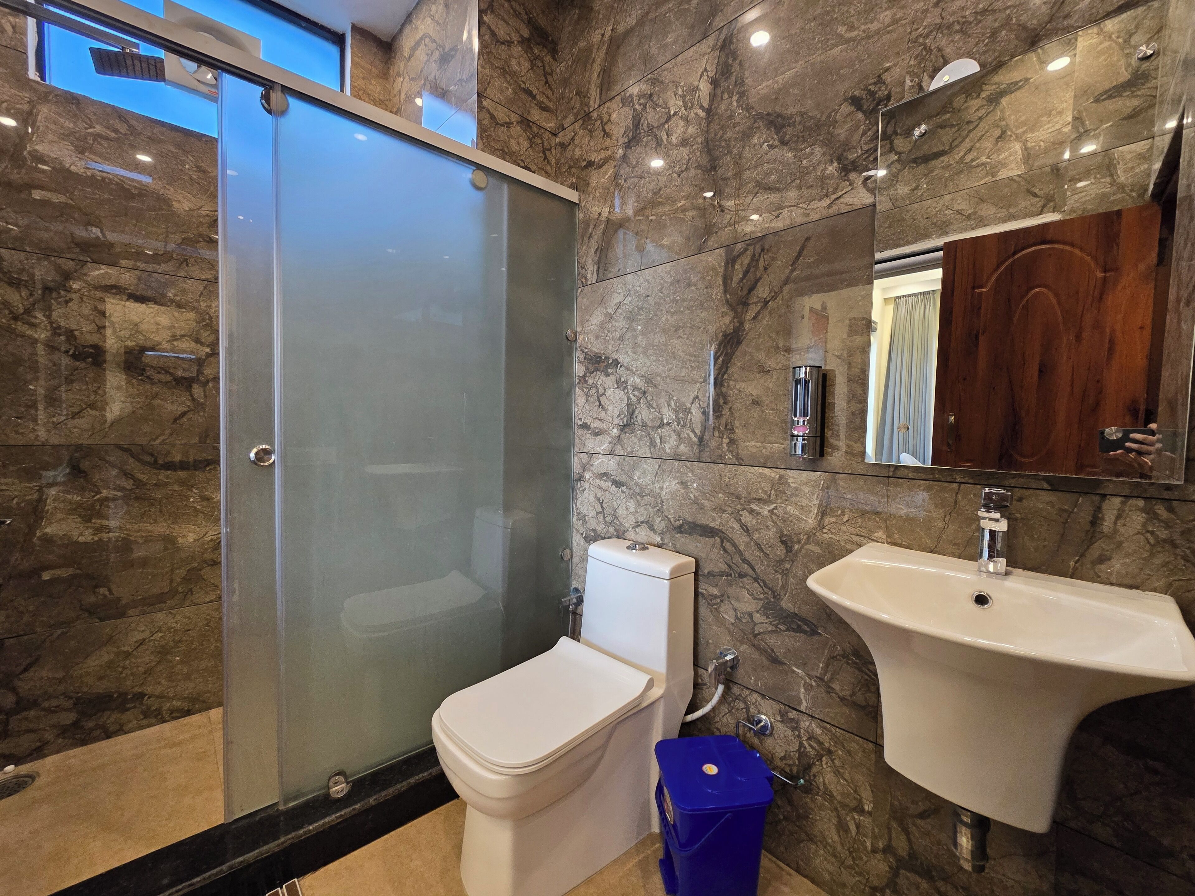 A modern bathroom with a glass-enclosed shower, a white toilet, and a sink with a marble backsplash.
