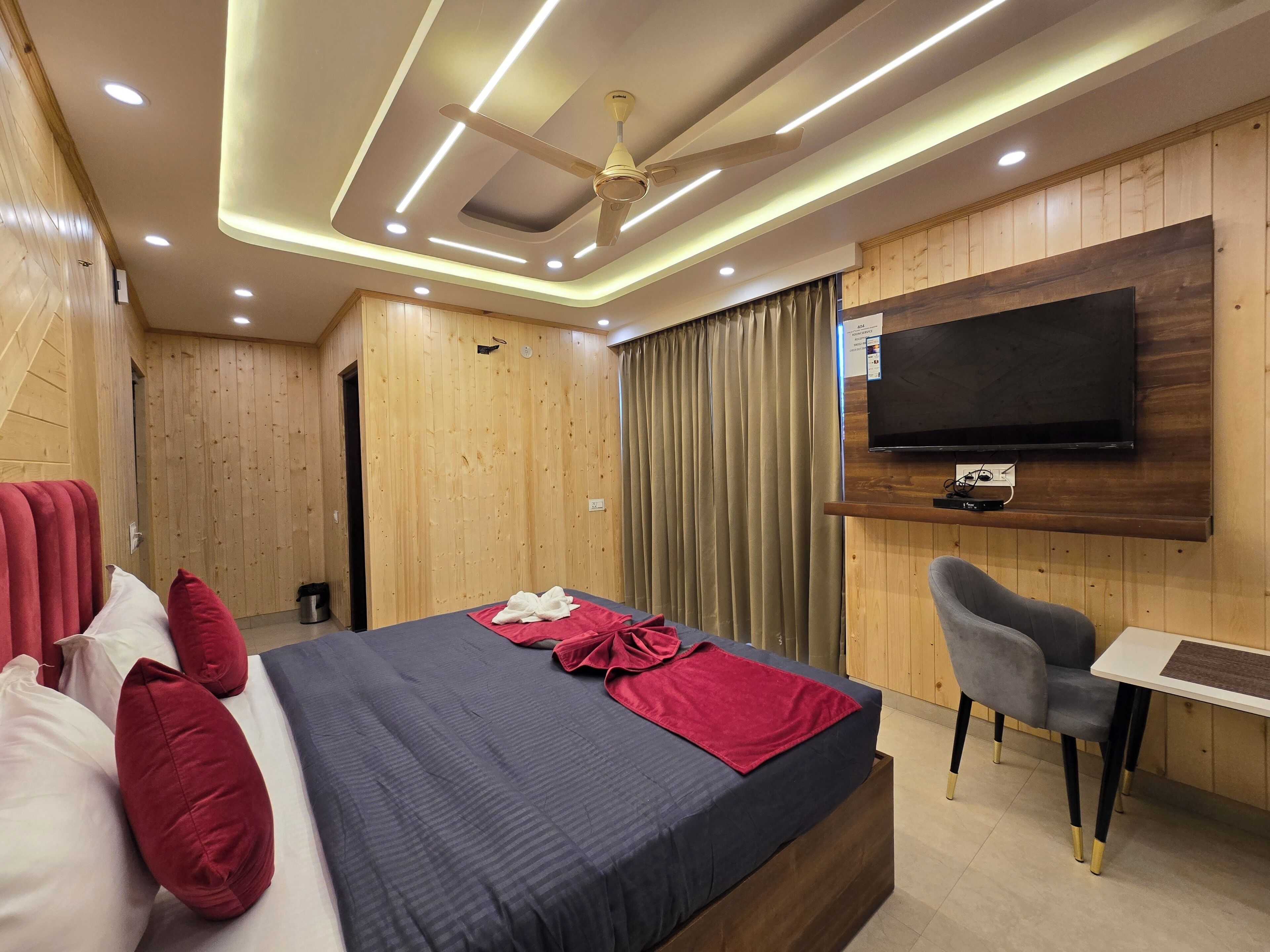 A modern hotel room with a large bed, a desk, a chair, a ceiling fan, and a TV mounted on the wall.