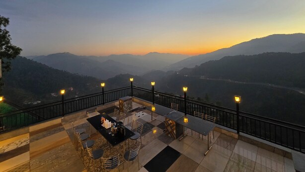 A terrace with a table and chairs, overlooking a valley with distant mountains. - Hotel Divshikha (Kasauli)
