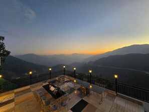 A terrace with a table and chairs, overlooking a valley with distant mountains. - Hotel Divshikha (Kasauli)