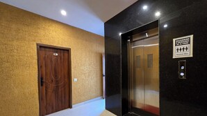 A hallway with a wooden door labeled "30", an elevator with a sign indicating a maximum of 4 persons at a time, and a red carpet leading to the elevator. - Hotel Divshikha (Kasauli)