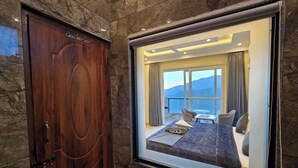 A hotel room with a large bed, a dining table, and a view of mountains through the window. - Hotel Divshikha (Kasauli)