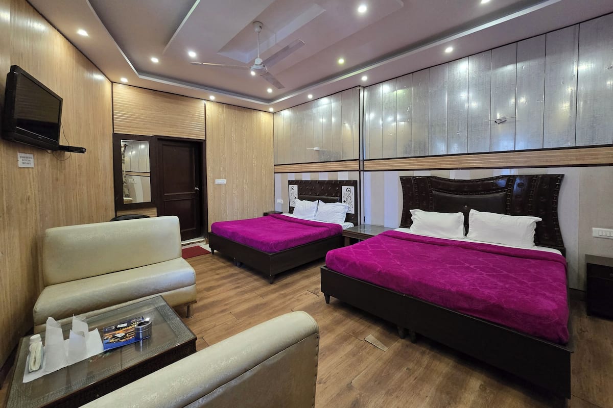 A hotel room with two beds, a sofa, a TV, and wooden paneling.