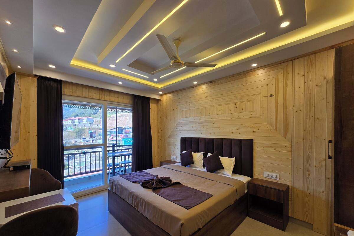 A hotel room with a bed, a desk, a chair, and a balcony with a view of buildings.
