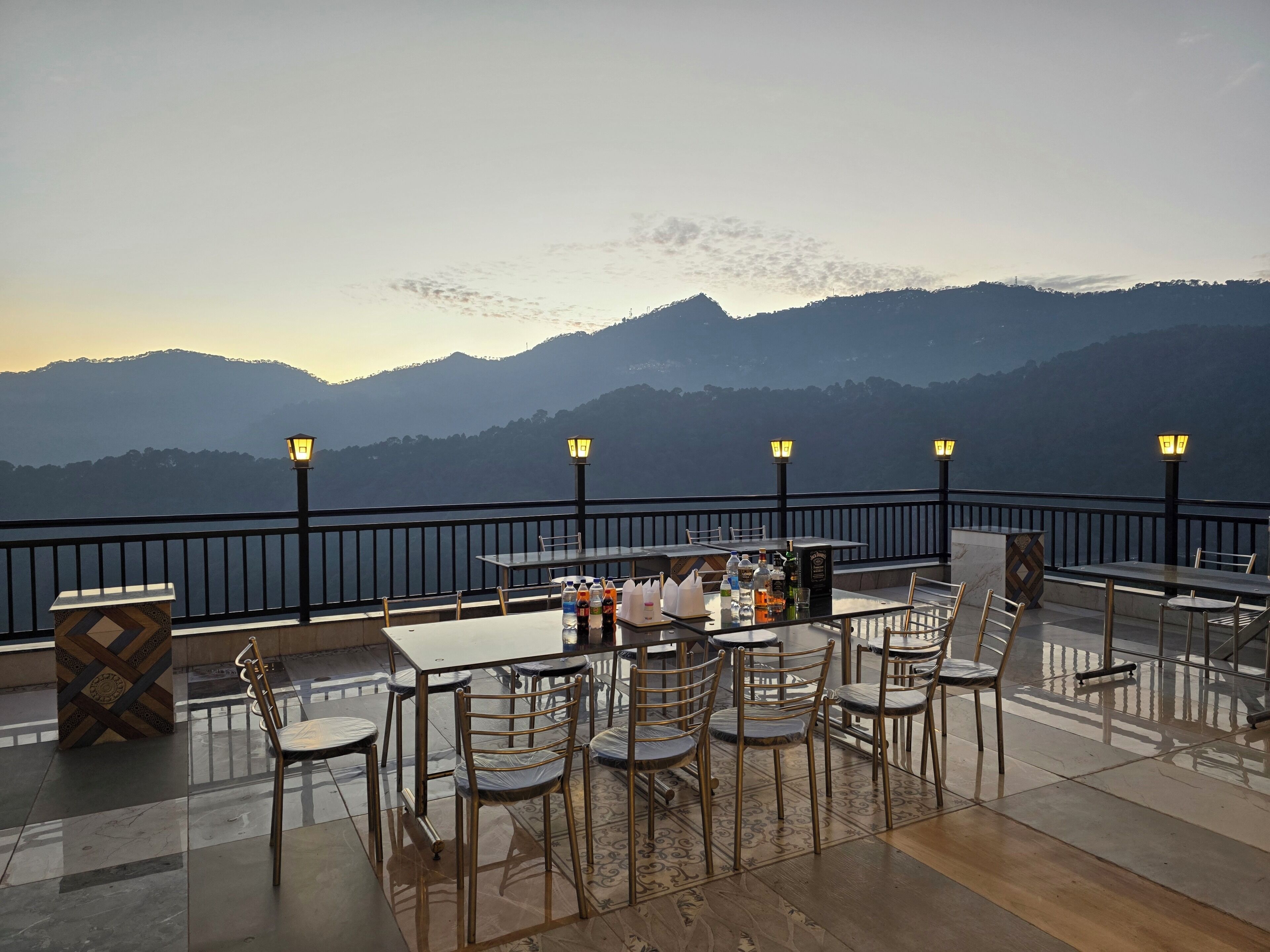 Una terraza con mesas y sillas, vista a montañas y una barandilla.