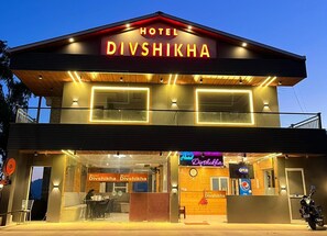 Un hotel llamado Divshikha, con fachada moderna, señalización iluminada y una entrada visible.