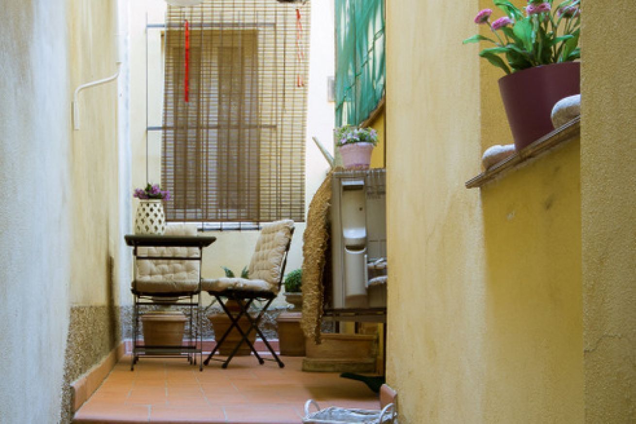 A narrow outdoor space with a chair, a small table, and a potted plant.