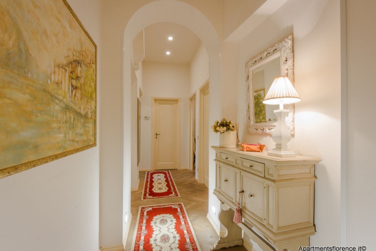 A hallway with a cream-colored cabinet, a mirror, and a red and white patterned rug.