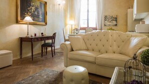 Una sala de estar con un sofá color beige, un escritorio de madera, una silla y una mesa de centro de vidrio.