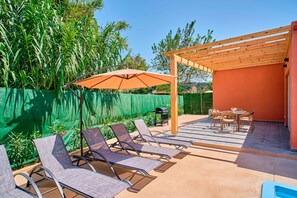 Une terrasse avec des chaises longues, une pergola en bois et une table avec des chaises.