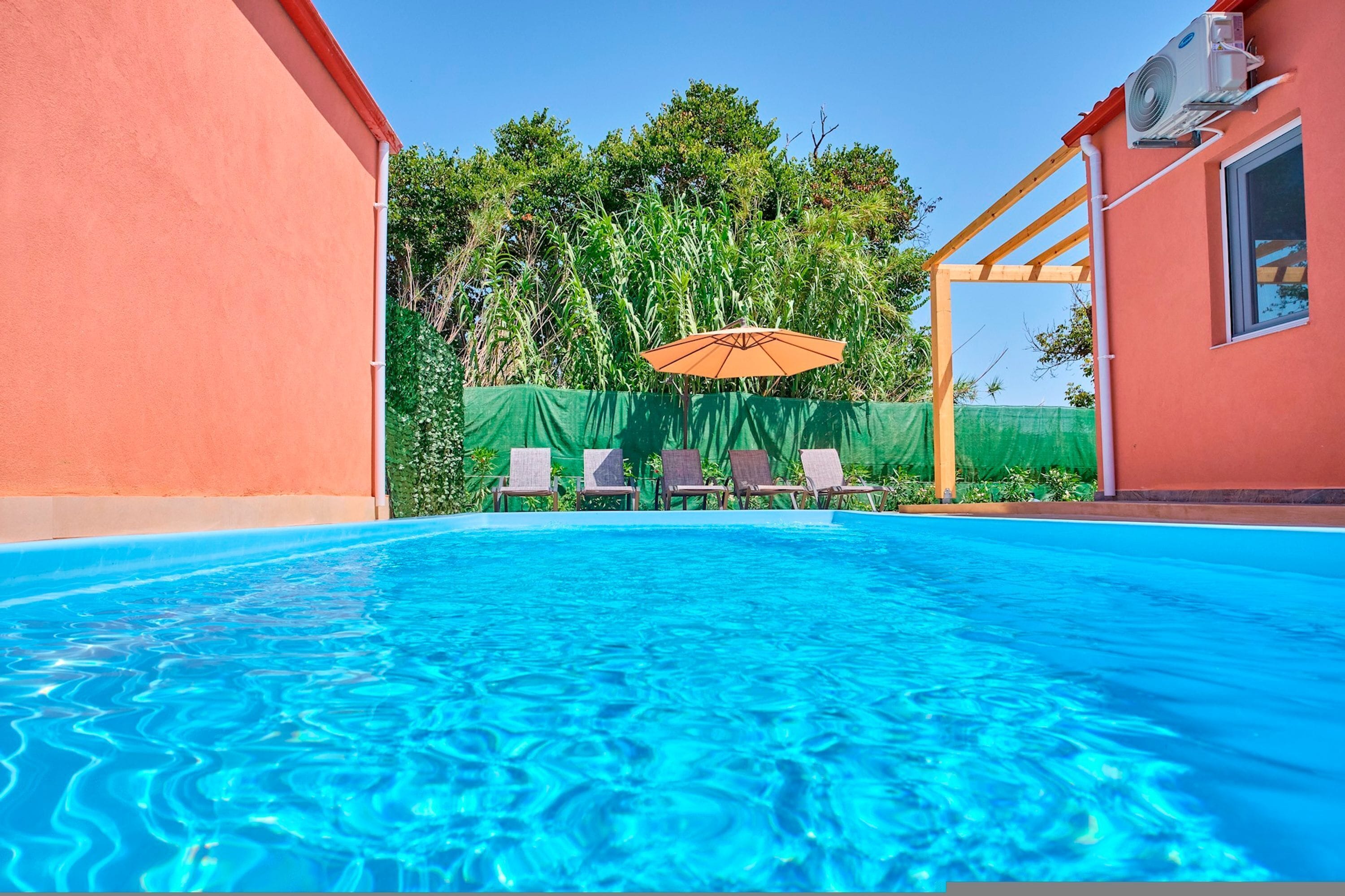 Ein Swimmingpool mit klarem, blauem Wasser, umgeben von einer Holzpergola und einem grünen Zaun.