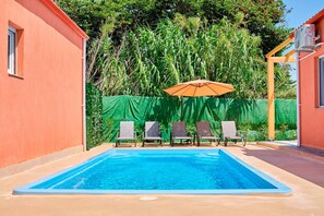 Ein rechteckiger Pool mit vier Liegestühlen und einem Sonnenschirm in der Mitte.