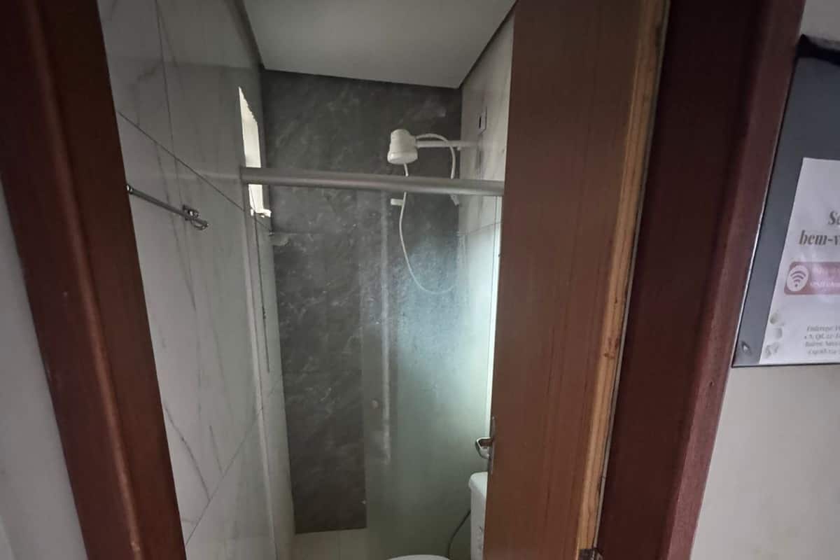 Ein schmales Badezimmer mit Toilette, Duschbereich und sichtbarem Türrahmen.