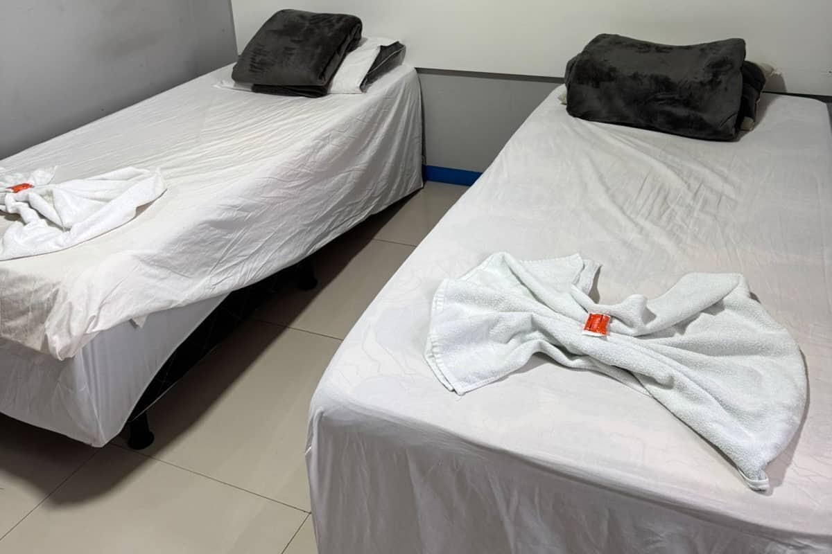 Zwei Einzelbetten mit weißen Laken und dunklen Kissen in einem Zimmer mit grauen Wänden und einem weißen Kopfteil.