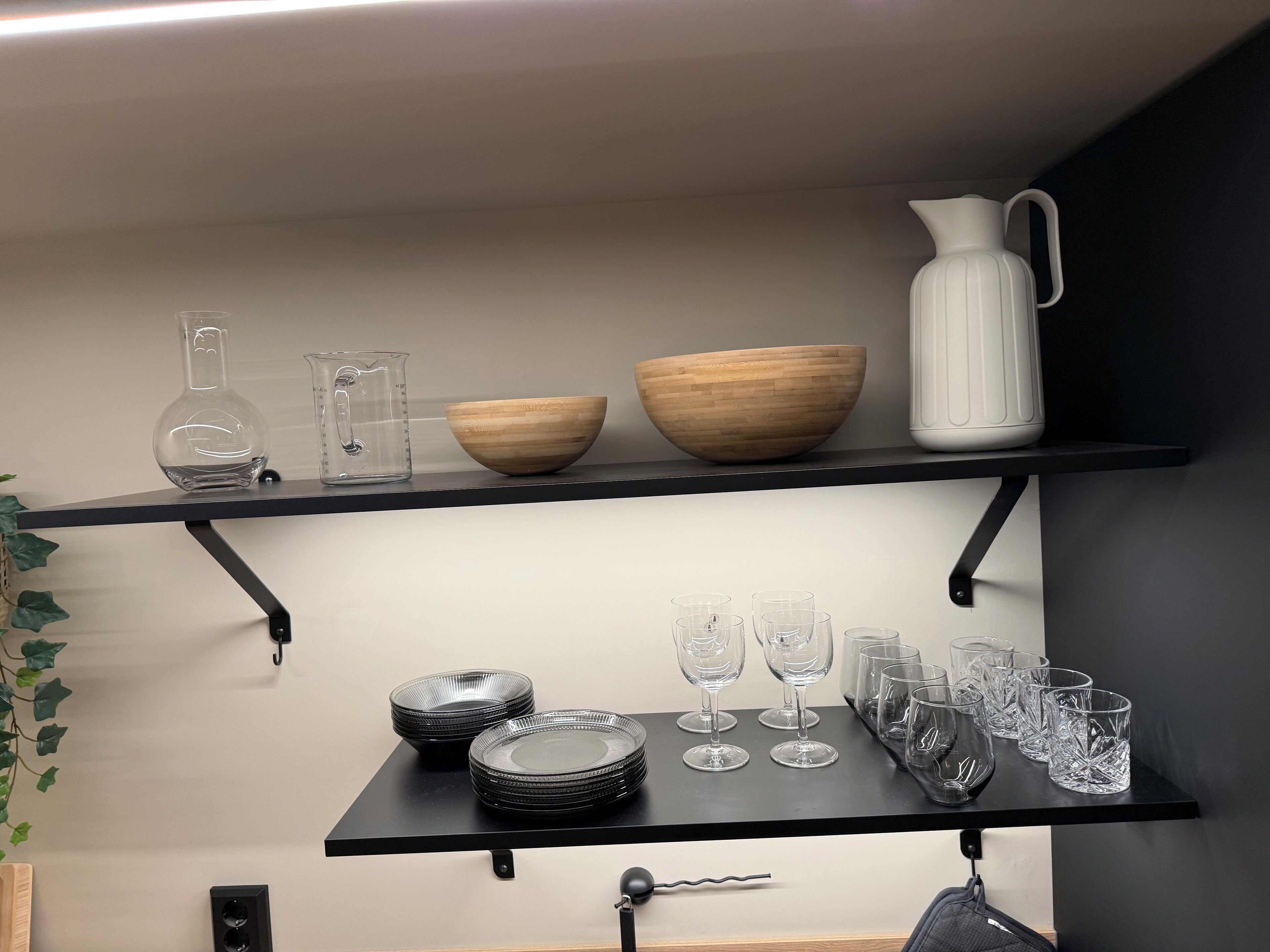 Une étagère de cuisine avec de la verrerie, un saladier en bois et un pichet blanc.