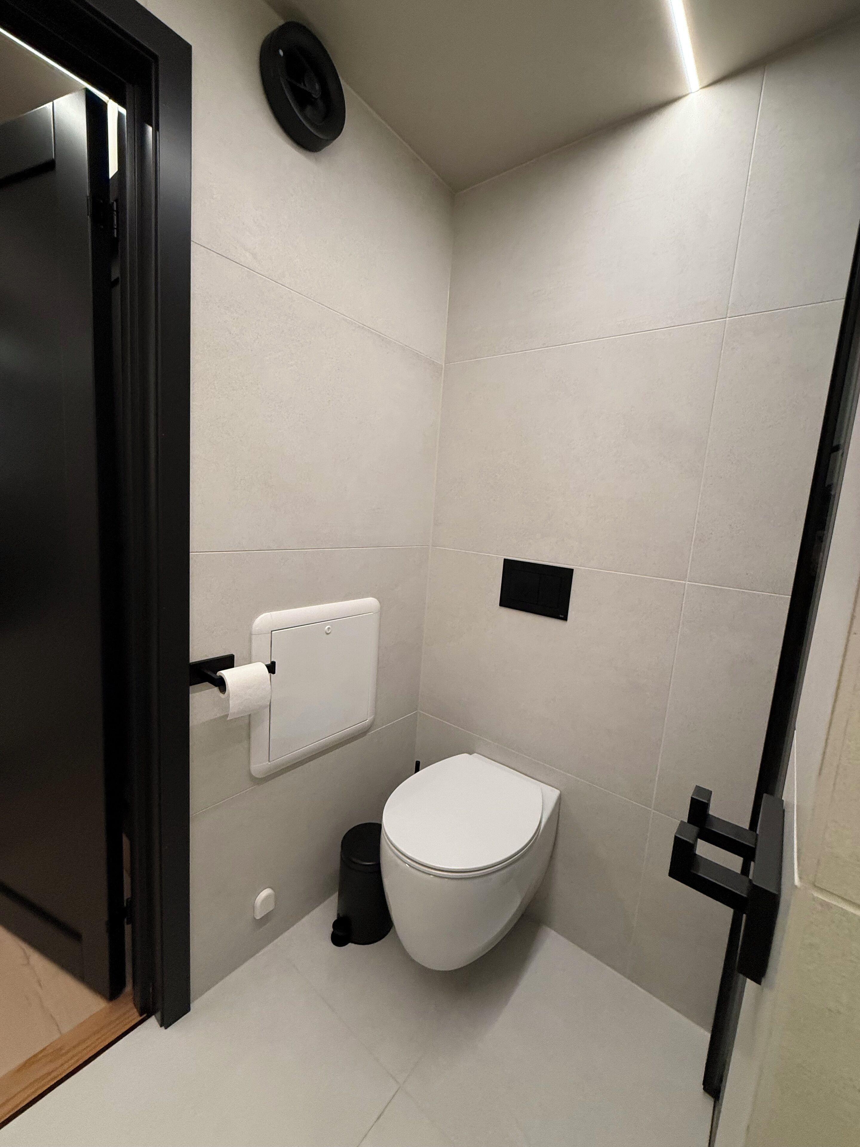 Ein kleines, modernes Badezimmer mit Toilette, Mülleimer und Handtuchspender.
