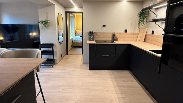 A modern kitchen with a wooden countertop, black cabinets, and a built-in oven. There is a dining area with a table and chairs, and a mirror on the wall. - Adorable 2-bedroom apartment in Telemark (Telemark)