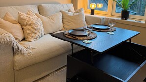 A living room with a sofa, a coffee table, and a window with a view of trees and a house. - Adorable 2-bedroom apartment in Telemark (Telemark)