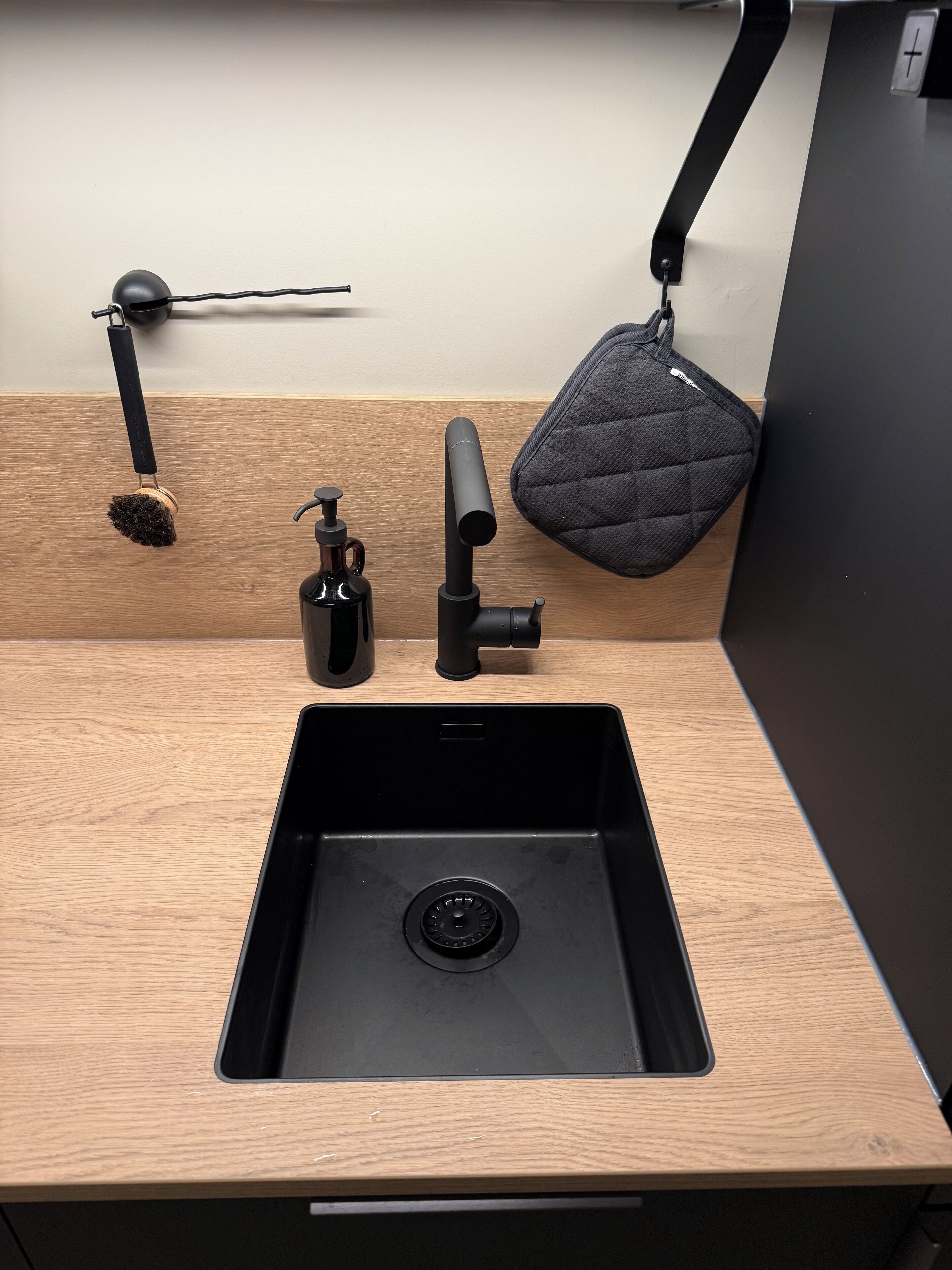Une cuisine moderne avec un plan de travail en bois, un évier noir, un distributeur de savon et un robinet noir.