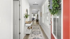 A hallway with a white door, a wooden console table with a mirror, a patterned rug, and a hanging plant. - Luxury New Build in Cherry Grove - Beach and Golf Destination (North Myrtle Beach)