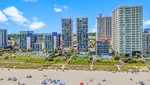 Ein Strandhotel mit mehreren Hochhäusern, einem Sandstrand und einem gepflegten Gartenbereich.