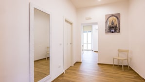A hallway with wooden flooring, white walls, a white-framed mirror, a door, and a chair. - Muzy Flat at Capuana by Napoliapartments (Naples)