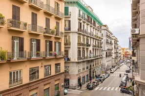 A multi-story building with balconies, a cobblestone street, and parked cars. - Muzy Flat at Capuana by Napoliapartments (Naples)