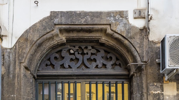 A black metal gate with a decorative arch, set in a stone wall with a number plate. - Muzy Flat at Capuana by Napoliapartments (Naples)
