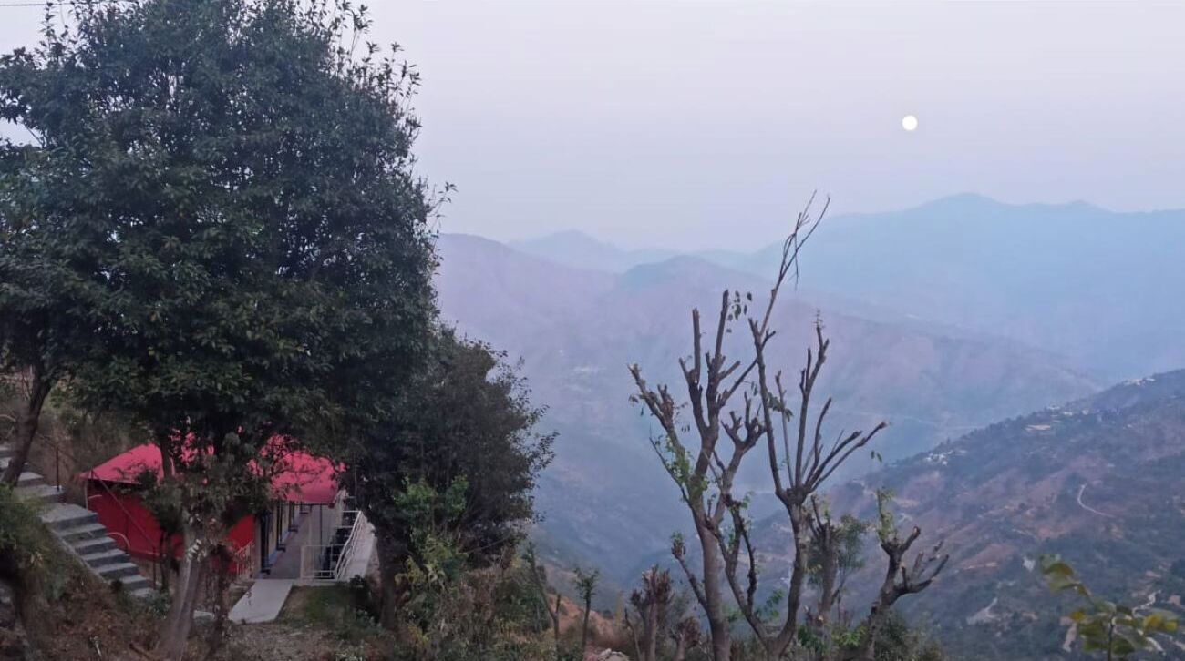 Un paisaje montañoso con un edificio de tejados rojos y una escalera que asciende.