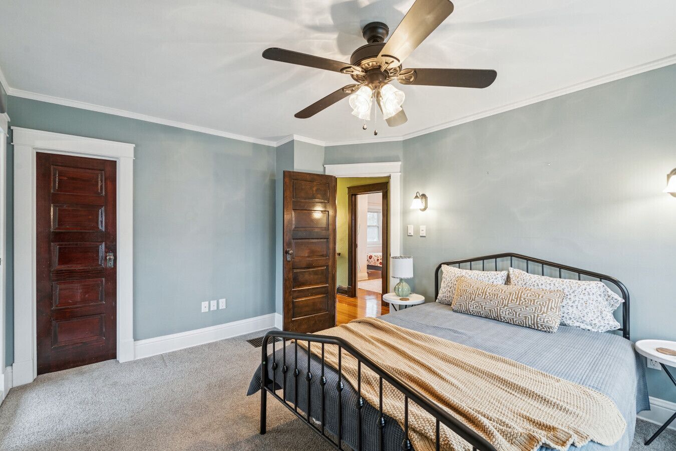 A bedroom with a bed, a ceiling fan, a nightstand, and a door.