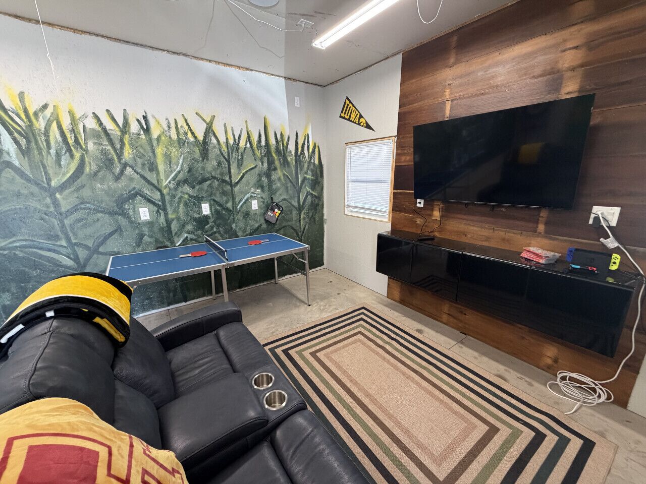 Ein Zimmer mit Tischtennisplatte, einer Couch, einem Fernseher und einem Wandgemälde.