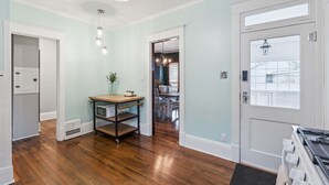 A hallway with a wooden floor, a white door, and a dining area visible through an open door.