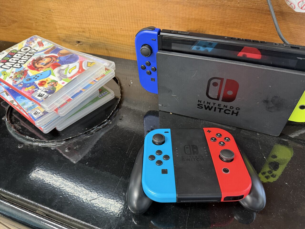 A Nintendo Switch console with two Joy-Con controllers, a game case, and a plastic storage box.