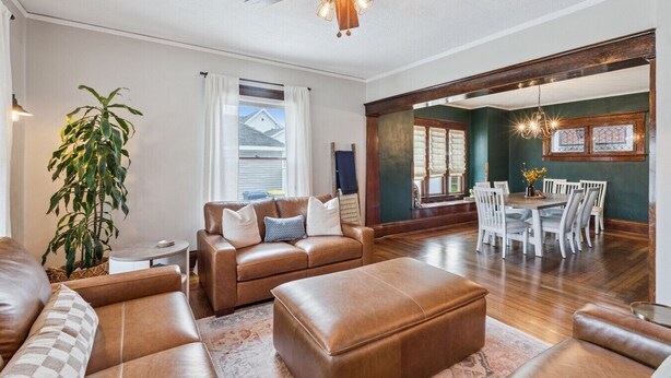 A spacious living room with a brown leather sofa, a dining area with white chairs, and a ceiling fan.