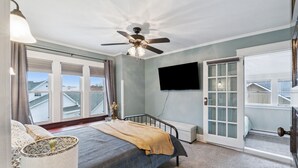 A bedroom with a bed, a ceiling fan, a TV, and a view of the outside.