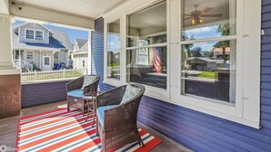 A covered porch with wicker furniture and a striped rug. - Charming Downtown Pella Cottage | Epic Game Room | Walk to Shops & Restaurants (Pella)