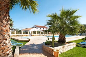 Un espace piscine avec des chaises longues, un palmier et un bâtiment doté d’un toit en tuiles.
