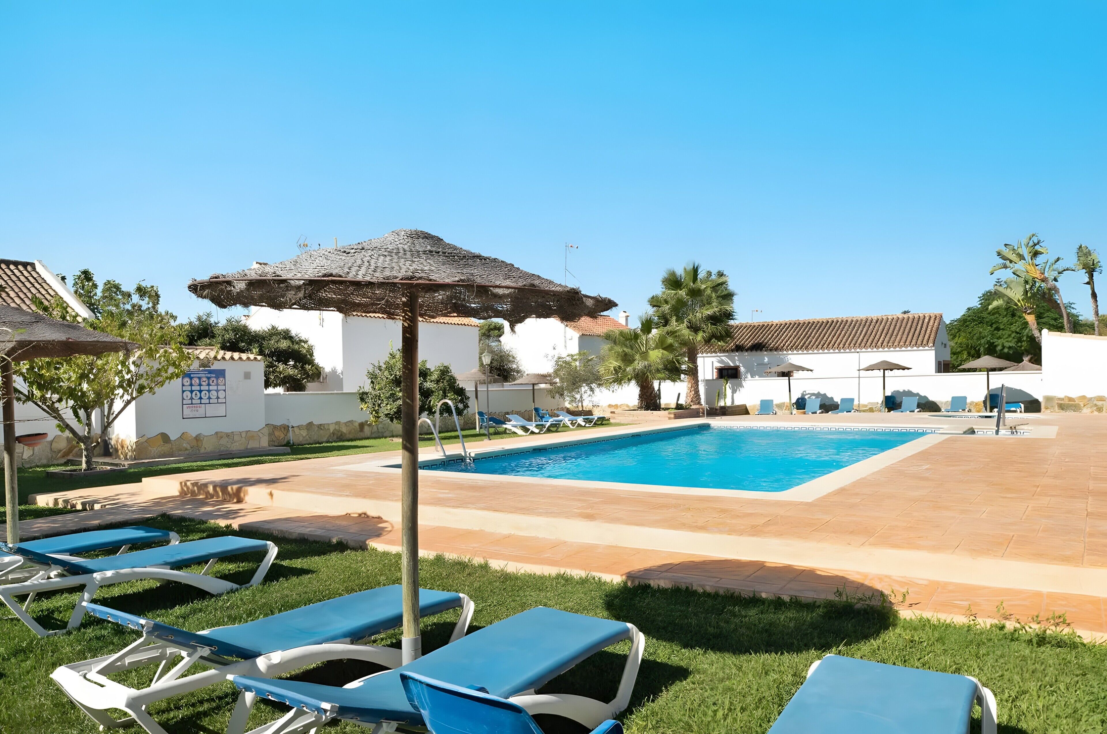 A swimming pool with lounge chairs, a shaded area, and a building with a tiled roof.