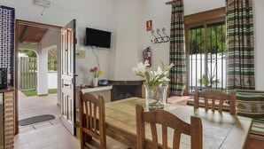 A dining area with a wooden table and chairs, a TV mounted on the wall, and a fire extinguisher. - Holiday Home 'Miguelin 2' with Shared Pool, Wi-Fi and Air Conditioning (Zahora)