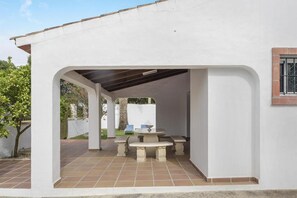 A covered patio area with a table and chairs, a tiled floor, and a white wall. - Holiday Home 'Miguelin 2' with Shared Pool, Wi-Fi and Air Conditioning (Zahora)