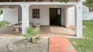 A covered outdoor seating area with tables and chairs, a small palm tree, and a door leading to an interior space. - Holiday Home 'Miguelin 1' with Shared Pool, Wi-Fi and Air Conditioning (Zahora)