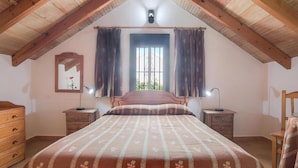 A bedroom with a wooden ceiling, a bed with a floral bedspread, two bedside tables with lamps, a dresser, and a window with curtains. - Holiday Home 'Miguelin 1' with Shared Pool, Wi-Fi and Air Conditioning (Zahora)