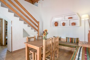A dining area with a wooden table and chairs, a staircase, a white shelf with pots, and a sofa with colorful cushions. - Holiday Home 'Miguelin 4' with Shared Pool, Wi-Fi and Air Conditioning (Zahora)