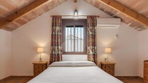 A bedroom with a sloped ceiling, a bed, two bedside tables with lamps, and a window with curtains. - Holiday Home 'Miguelin 5' with Shared Pool, Wi-Fi and Air Conditioning (Zahora)