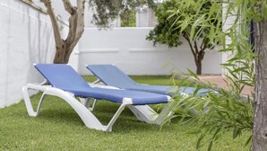 Two lounge chairs on a grassy lawn with a white wall and trees in the background. - Holiday Home 'Miguelin 5' with Shared Pool, Wi-Fi and Air Conditioning (Zahora)