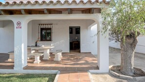 A covered patio with a table and chairs, a no dogs sign, and a tree. - Holiday Home 'Miguelin 8' with Shared Pool, Wi-Fi and Air Conditioning (Zahora)