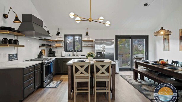 A modern kitchen with a central island, stainless steel appliances, and a dining area with a bench and table. - Lake Geneva House: Family Fun with Pool Table (Lake Geneva)