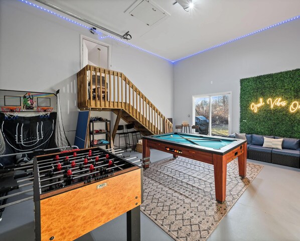 Una sala de estar moderna con mesa de fútbol, mesa de billar y una escalera.