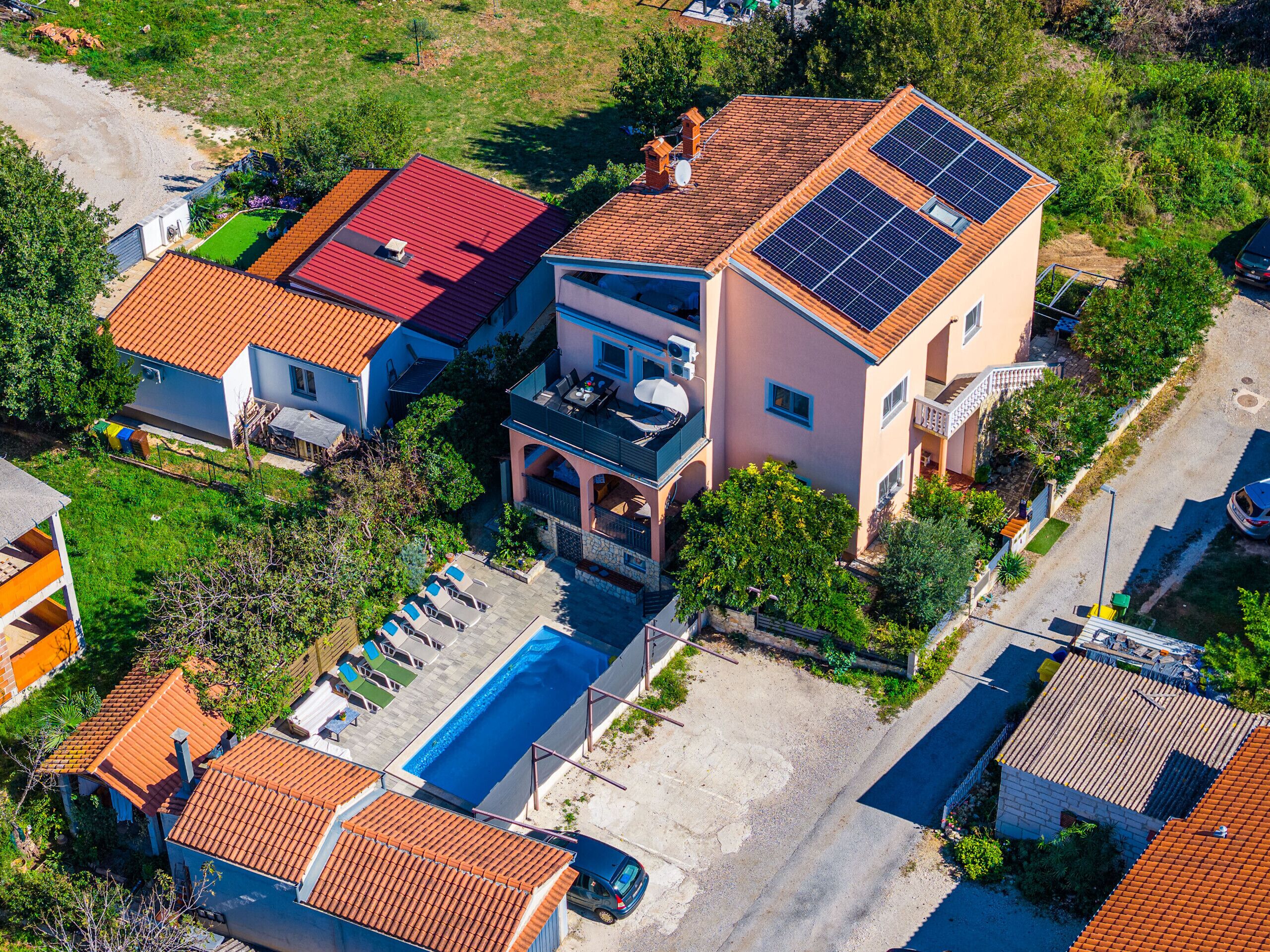Een woonhuis met een zwembad, zonnepanelen en een twee verdiepingen tellend gebouw met balkon.