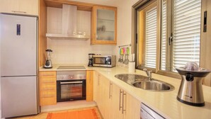 Eine kompakte Küche mit Kühlschrank, Herd, Mikrowelle, Spüle und einem Fenster mit Jalousien.